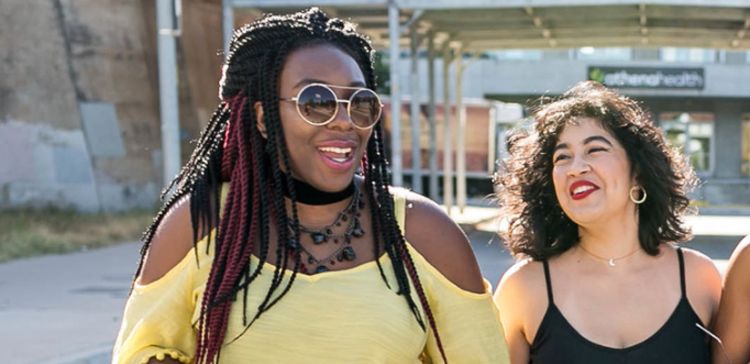 Editor April B a black woman with black and red crochet braids laughs with editor Leslie a Latina with shoulder length dark curls