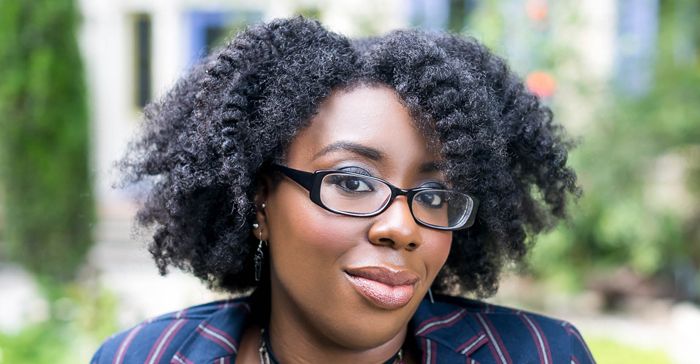 Editor April B a black woman with glasses and a fluffy twist out sits and smiles.