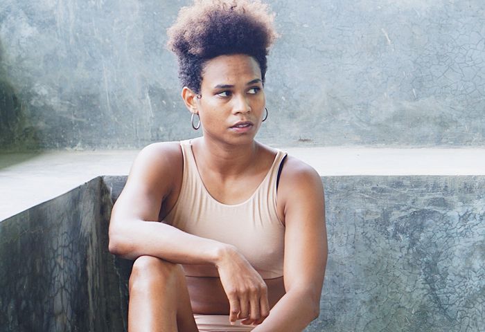 A black woman with a fade haircut and clearly grown out sides sits in a concrete stairwell looking pensive