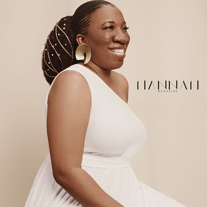 African-American woman sitting down with her hair braided and accessorized with beads and gold rope wearing a white dress