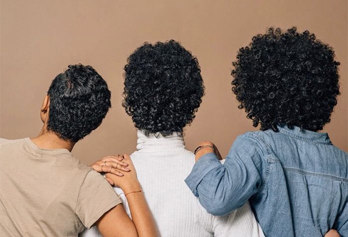 Three women with curly hair show off their hair texture standing arm and arm