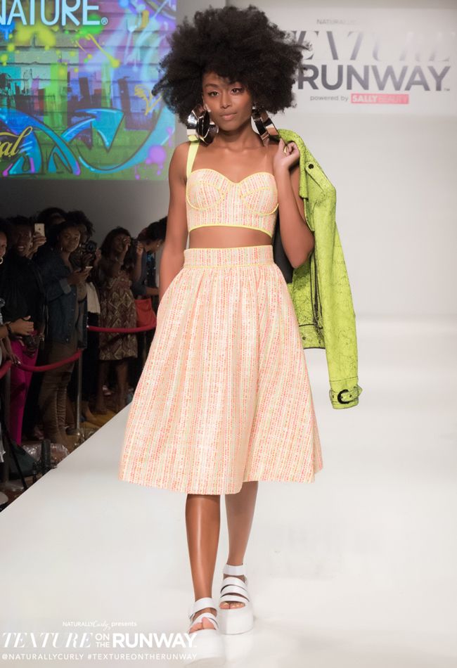 a black model walks the runway in an orange green and white color scheme that is an inversion of the previous model NaturallyCurly
