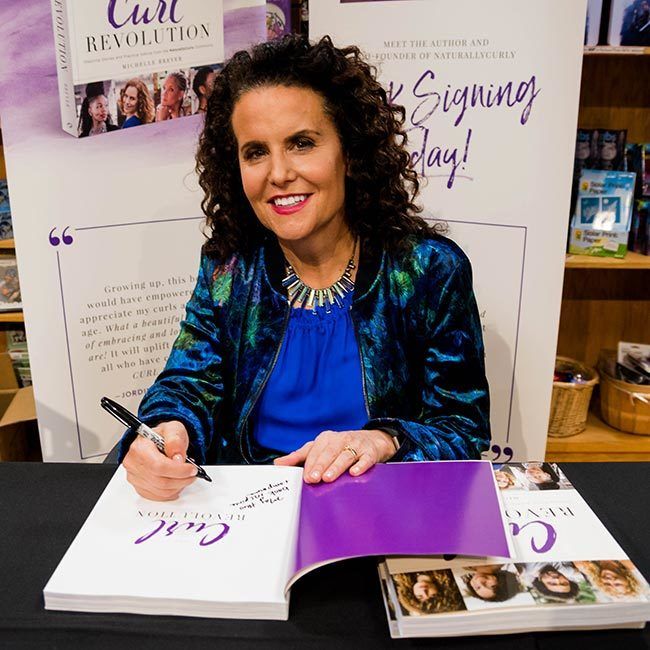 Author Michelle Breyer smiles at camera while signing a copy of her book The Curl Revolution at book signing event held in Austin, TX on October 3, 2017.