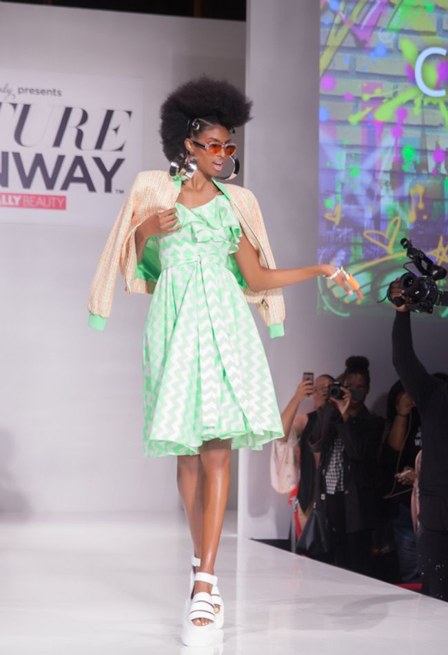 a black model in a mixed bantu knot and afro style walks the runway in neon green orange and bright white NaturallyCurly