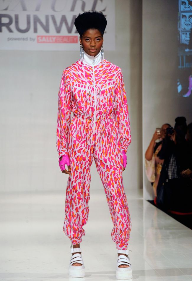 a black model in a neon pink and white jumpsuit faces the camera with a wry smile GettyImages Asset ID - 7901032
