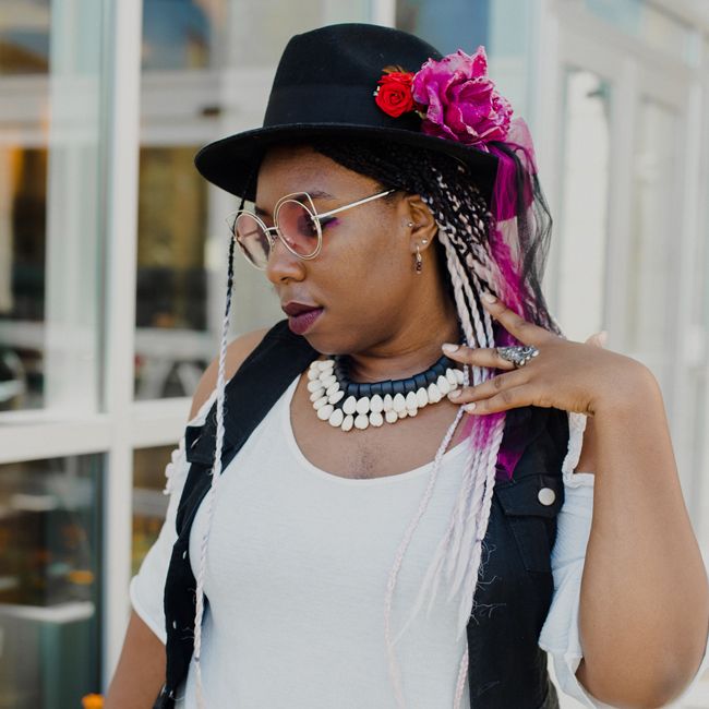 Editor April B strokes the ribbons coming off of her fedora and looks down wistfully