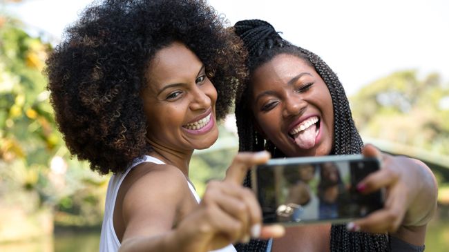 as a friendship matures we trade mannerisms The same afroed and braided women take another selfie, but now their expressions have switched!