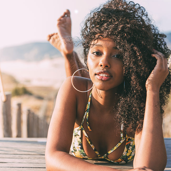 Beautiful young black woman lying down in a wooden foot bridge at the beach